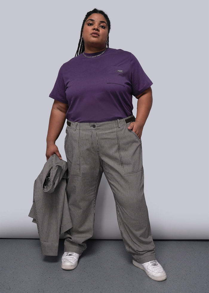 1X=Person wearing a purple t-shirt and striped pants holding a gray jacket against a plain background