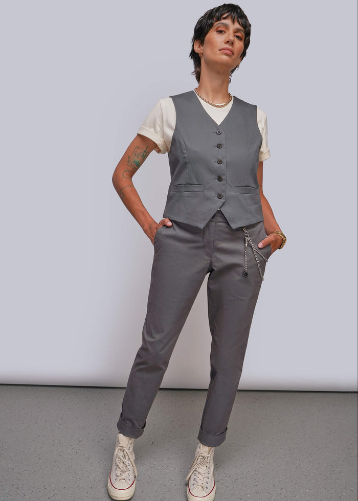 S=A model wearing a gray vest and matching gray trousers over a white t-shirt, styled with white sneakers, standing against a light gray studio background.