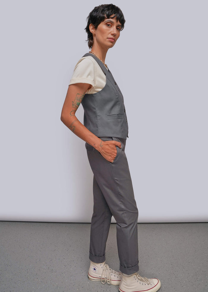 S=A model wearing a gray vest over a cream t-shirt, gray pants, and off-white high-top sneakers, standing against a light gray studio background.