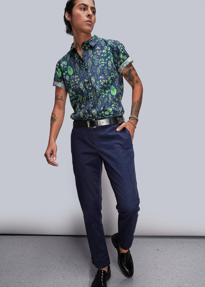 S=Person wearing a patterned shirt and navy pants against a plain background