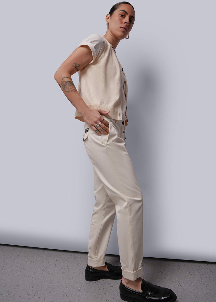 S=Person wearing a beige sweater vest and pants with black shoes against a plain background
