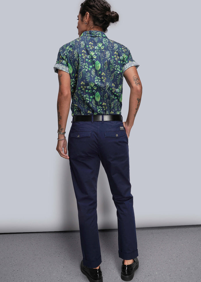 S=Person wearing a patterned shirt and navy pants against a plain background