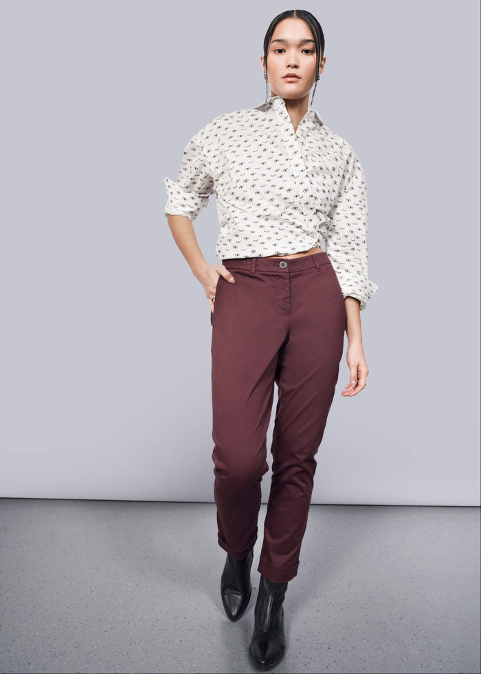 S=A person stands against a white backdrop wearing a patterned white shirt with convertible cuffs, The Essential Trouser in burgundy tapered-leg style, and black ankle boots. One hand is casually in a pocket, their expression neutral.