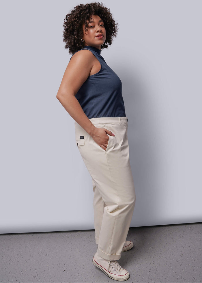 1X=Woman wearing a navy sleeveless top and beige pants against a plain background