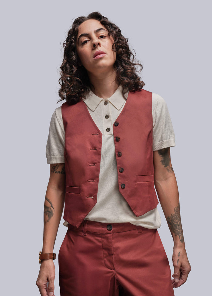 S=Person wearing a rust colored vest over a white sweater polo with a plain background
