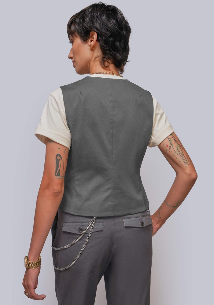 S=A model shown from the back wearing a dark gray sleeveless vest over a cream t-shirt and matching gray trousers with a silver chain detail at the back waist.