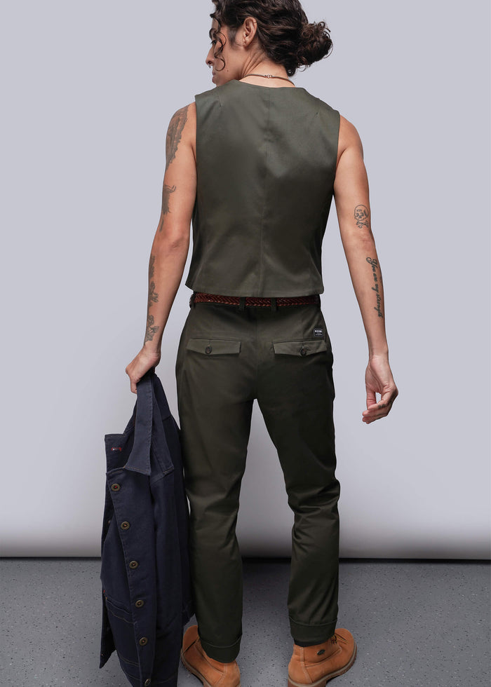 S=Person wearing a green sleeveless vest and pants holding a jacket against a plain background