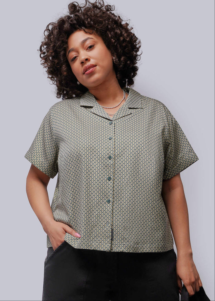 1X=Person wearing a green patterned shirt and black pants against a plain background