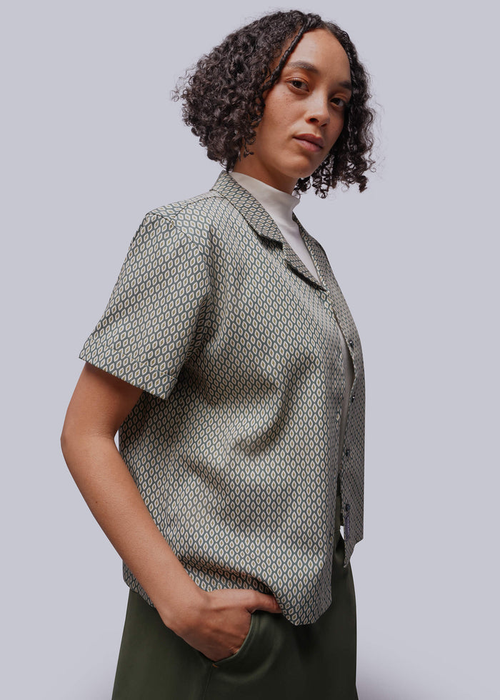 S=Woman wearing a patterned shirt with short sleeves against a plain background