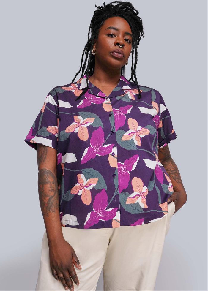 1X=Person wearing a purple floral patterned shirt against a gray background