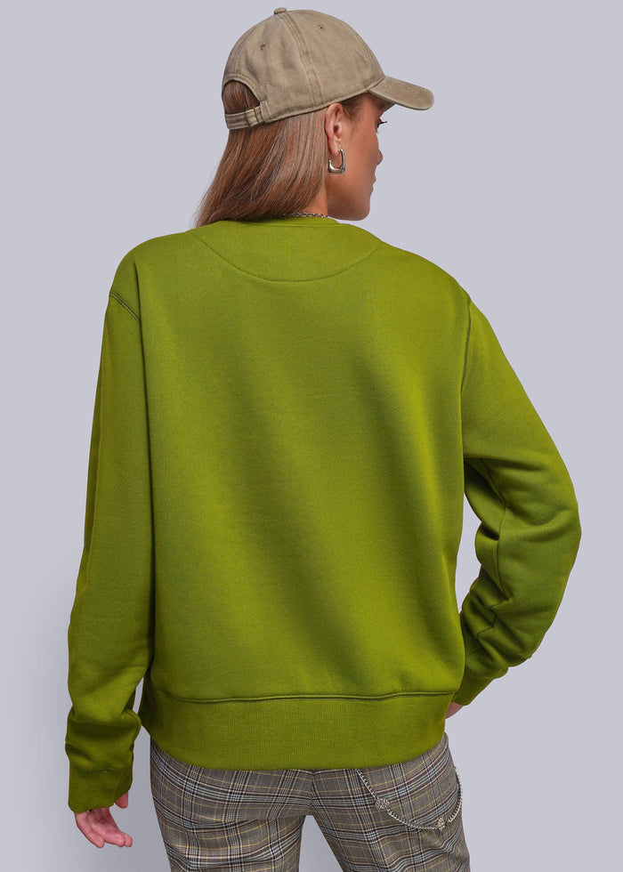 S=A person shown from the back wearing a green crewneck sweatshirt, a beige baseball cap, and plaid pants, set against a solid light gray background.