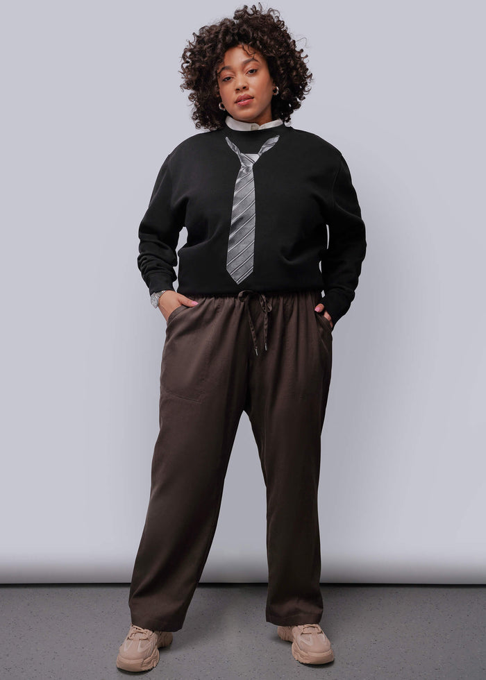 1X=Person wearing a black sweater, brown pants, and a striped tie against a plain background