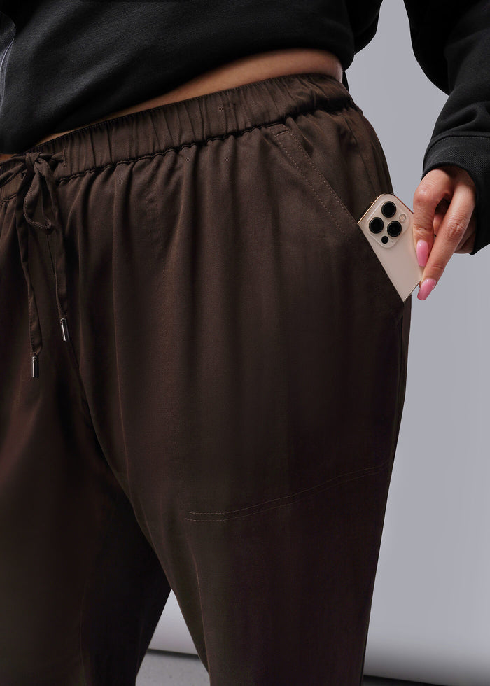 1X=Person wearing brown pants holding a phone with a gray background