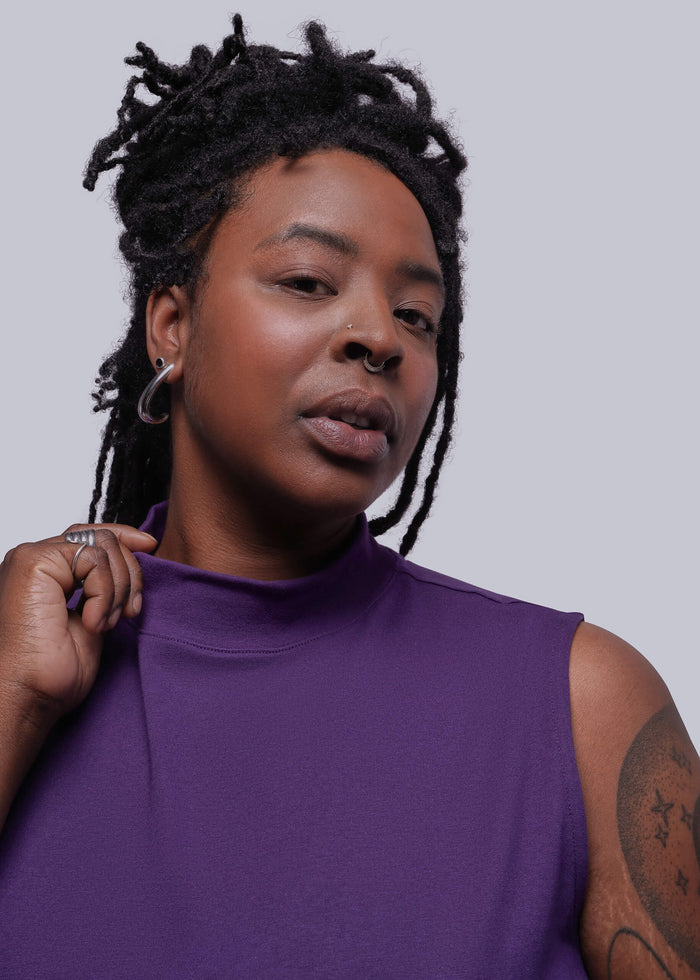 1X=Person wearing a purple sleeveless top against a plain background