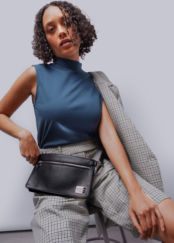 S=Woman holding a black handbag against a plain background