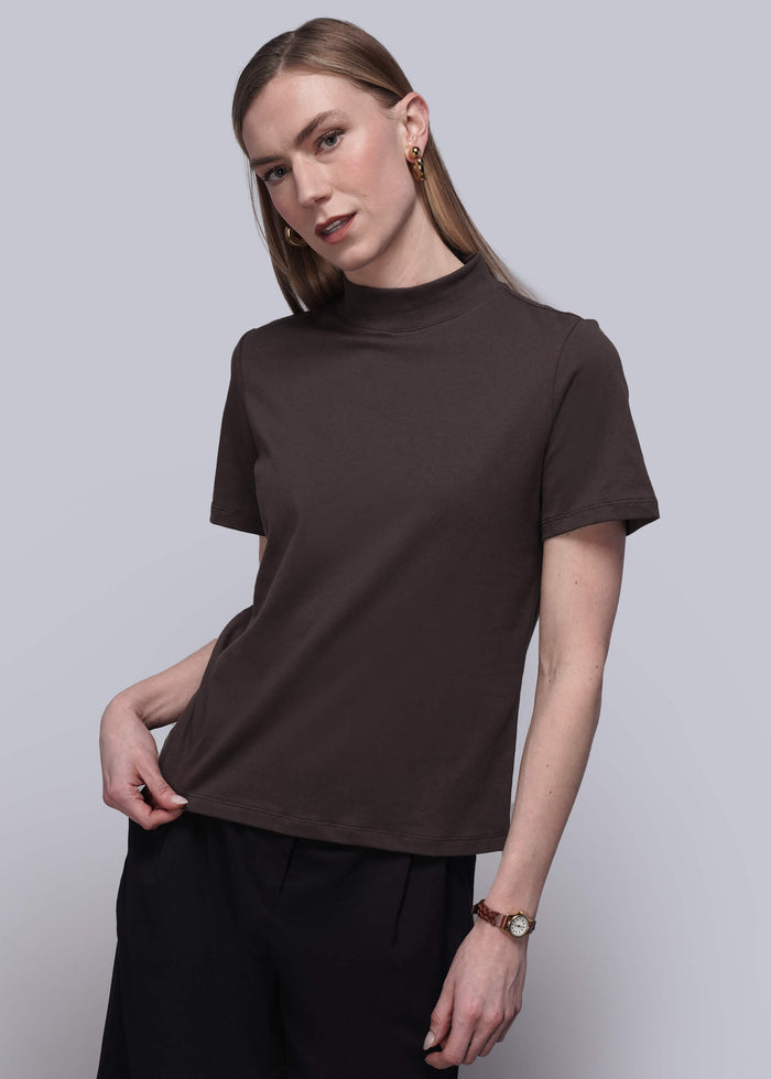 S=Woman wearing a brown t-shirt and black pants against a light gray background