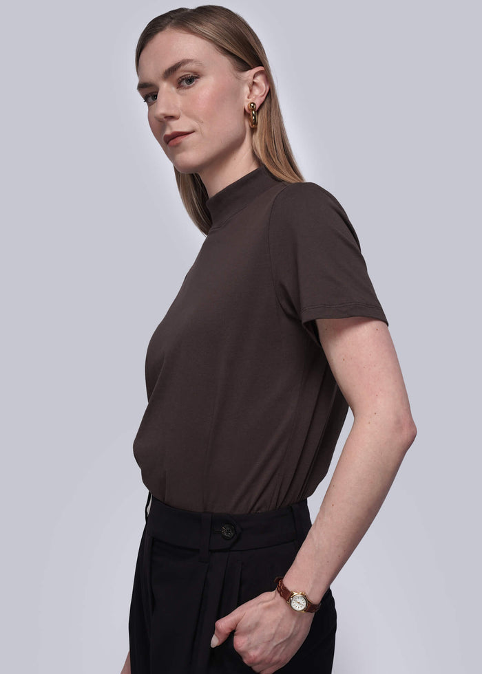 S=Woman wearing a brown top and black pants against a white background
