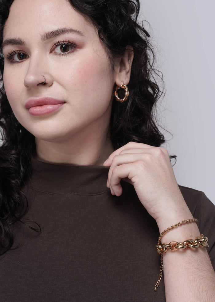 1X=Person wearing gold hoop earrings and brown t shirt against a neutral background