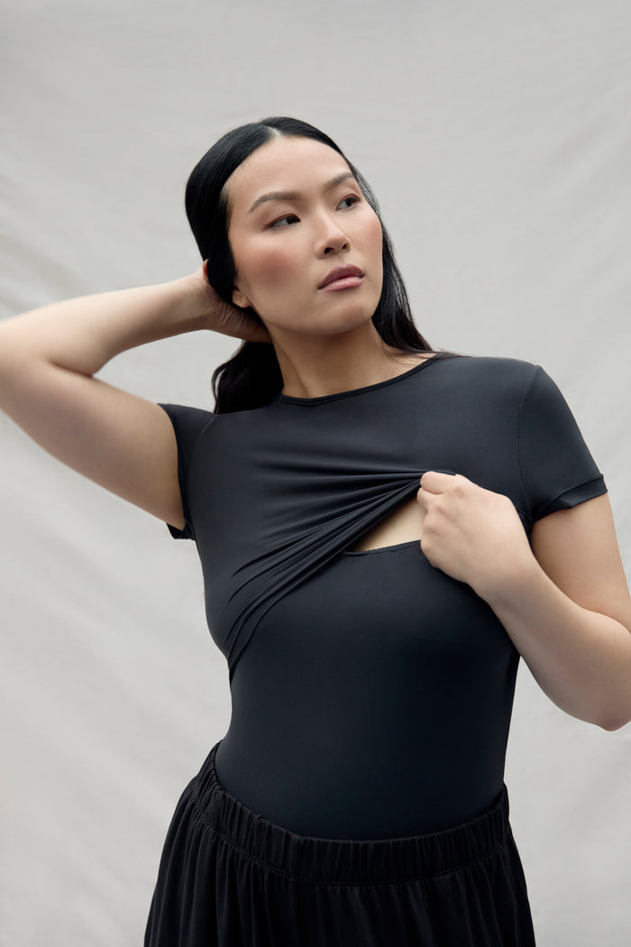 Woman wearing a black top with breast feeding access on a plain background