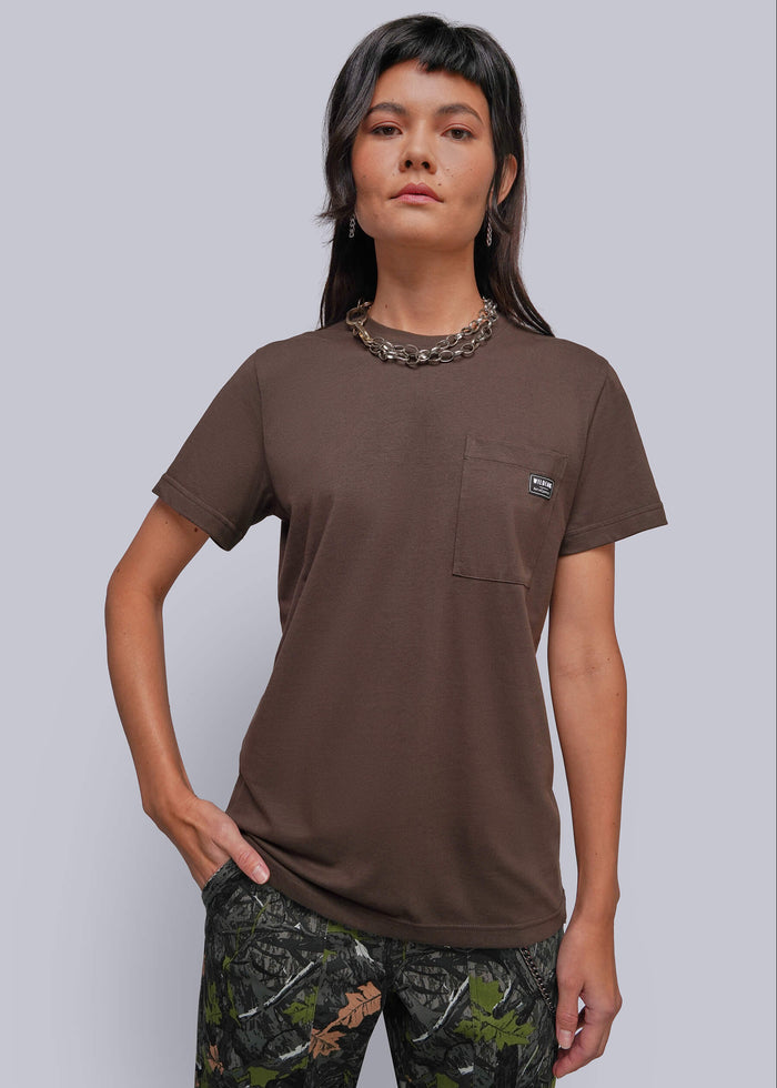 S=A woman modeling a brown short-sleeve pocket t-shirt with a small embroidered logo on the chest pocket, paired with camouflage pants, against a solid gray studio background.