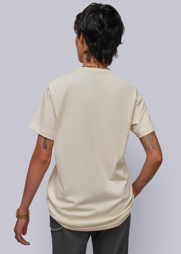 S=A person shown from the back wearing a cream-colored short-sleeve t-shirt and dark gray pants, set against a solid light gray background.