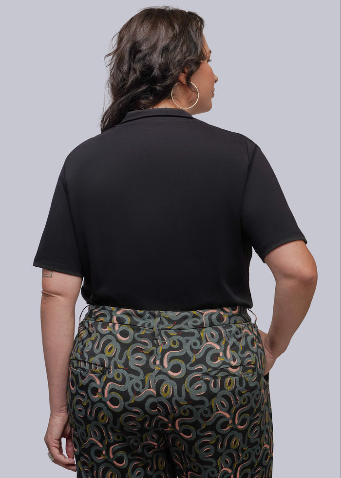 1X=A woman shown from the back wearing a black short-sleeve polo shirt and dark green patterned trousers.