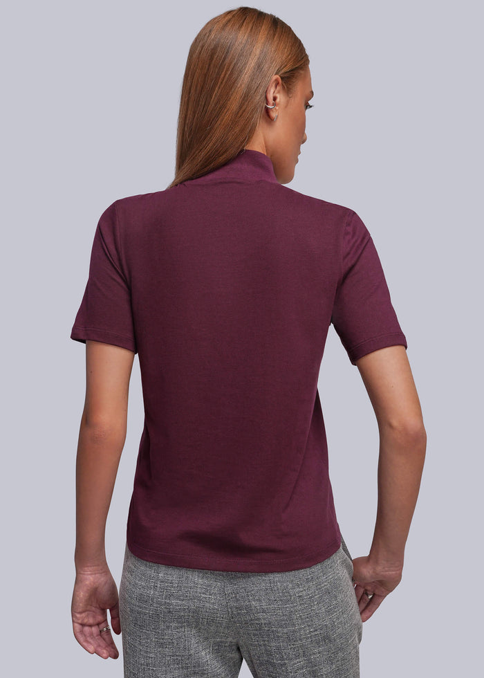 S=A woman shown from the back wearing a short-sleeve shirt in maroon and gray trousers, photographed against a solid light gray studio background.