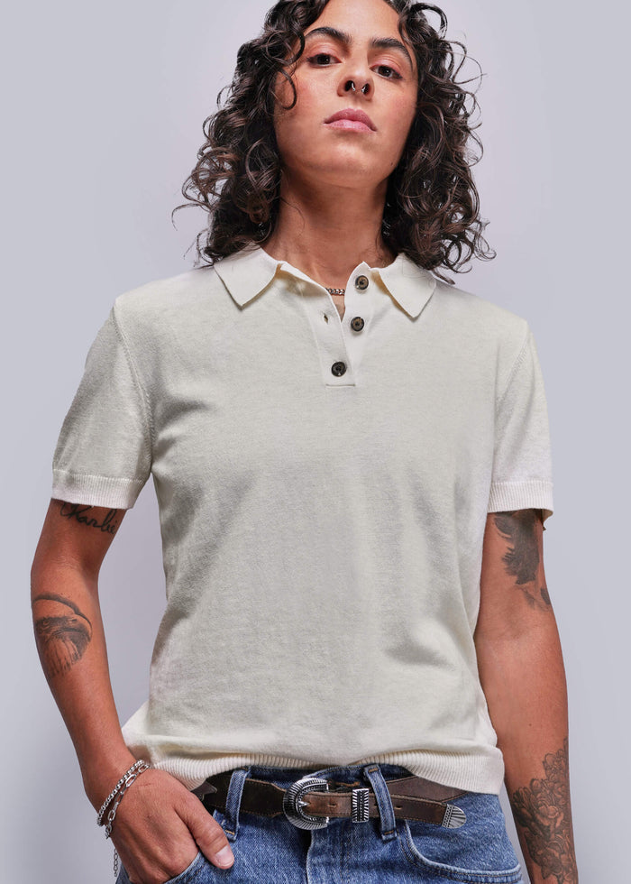S=Person wearing a light-colored polo shirt and jeans against a plain background