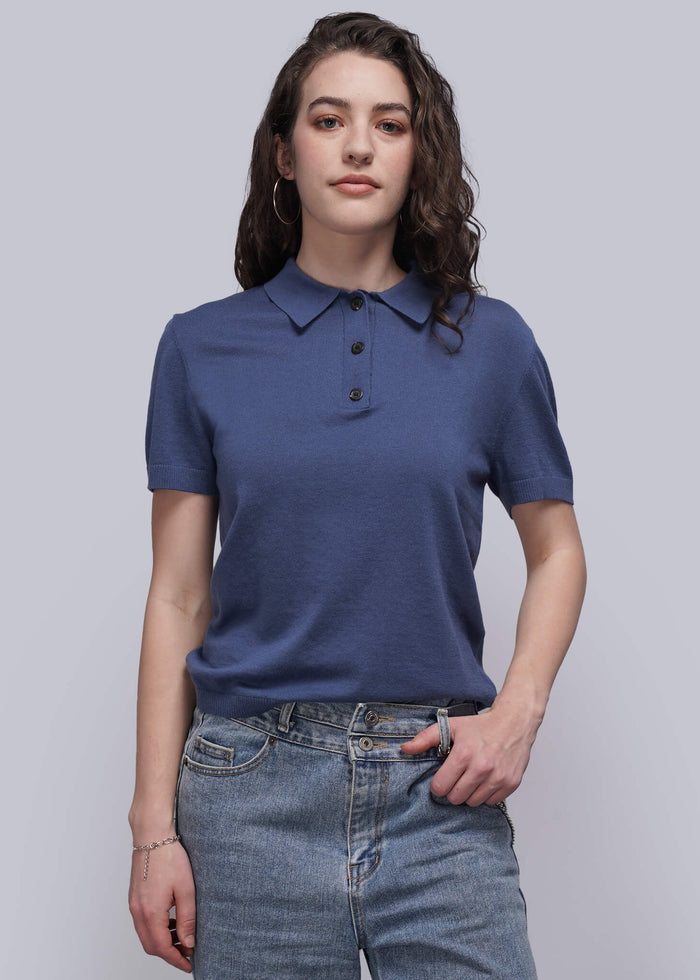 S=Woman wearing a blue polo shirt and jeans against a plain background