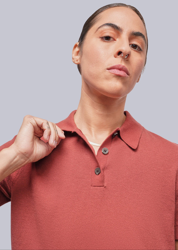 S=A close-up of a model wearing a short-sleeve polo shirt in a muted terracotta color, set against a solid light gray background.