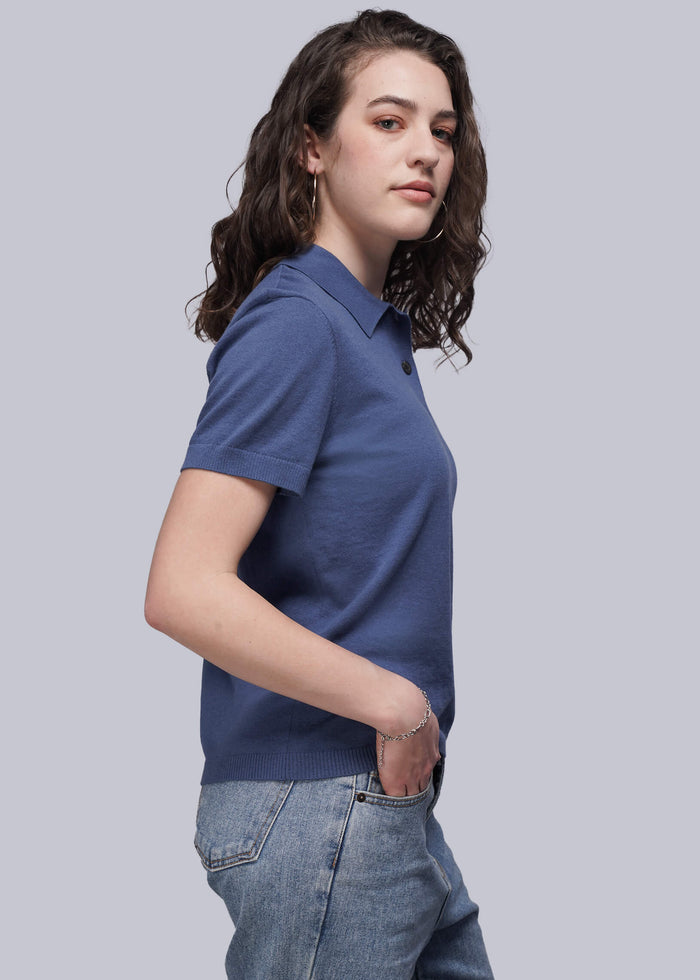 S=Woman wearing a blue polo shirt and jeans against a light gray background