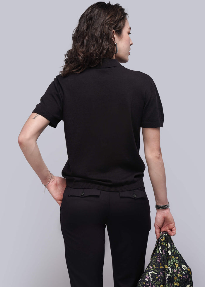 S=Person wearing a black outfit holding a floral-patterned jacket against a plain background