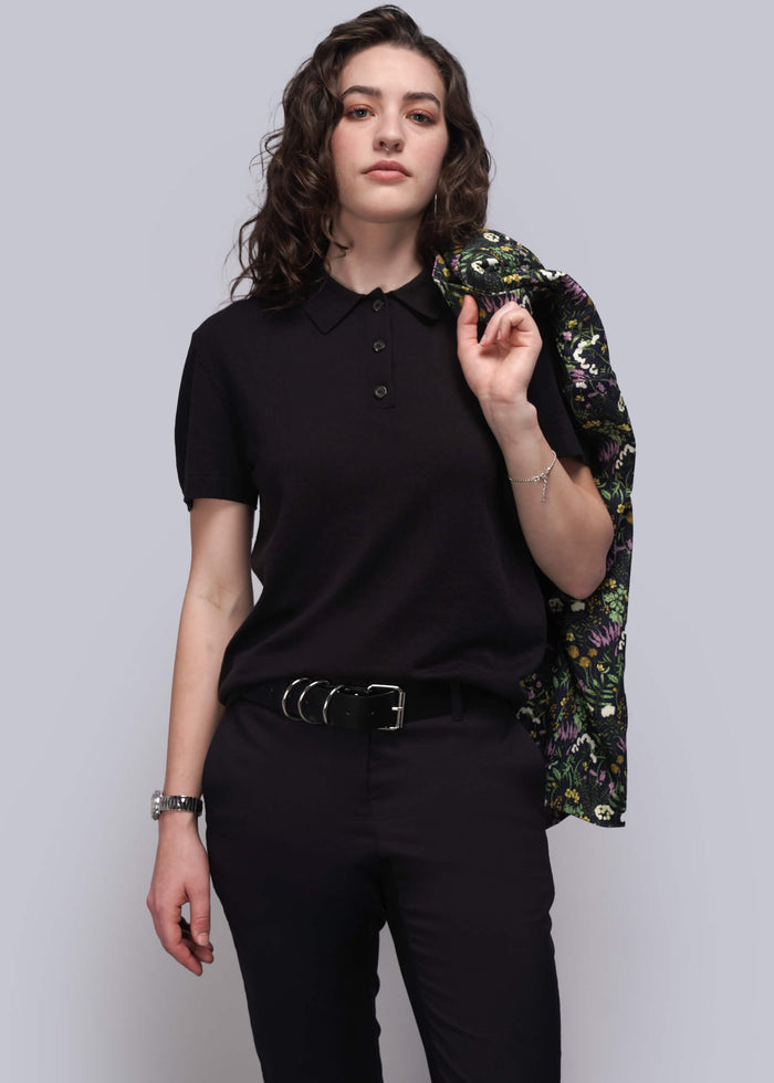 S=Person wearing a black sweater and pants with a floral jacket on a plain background