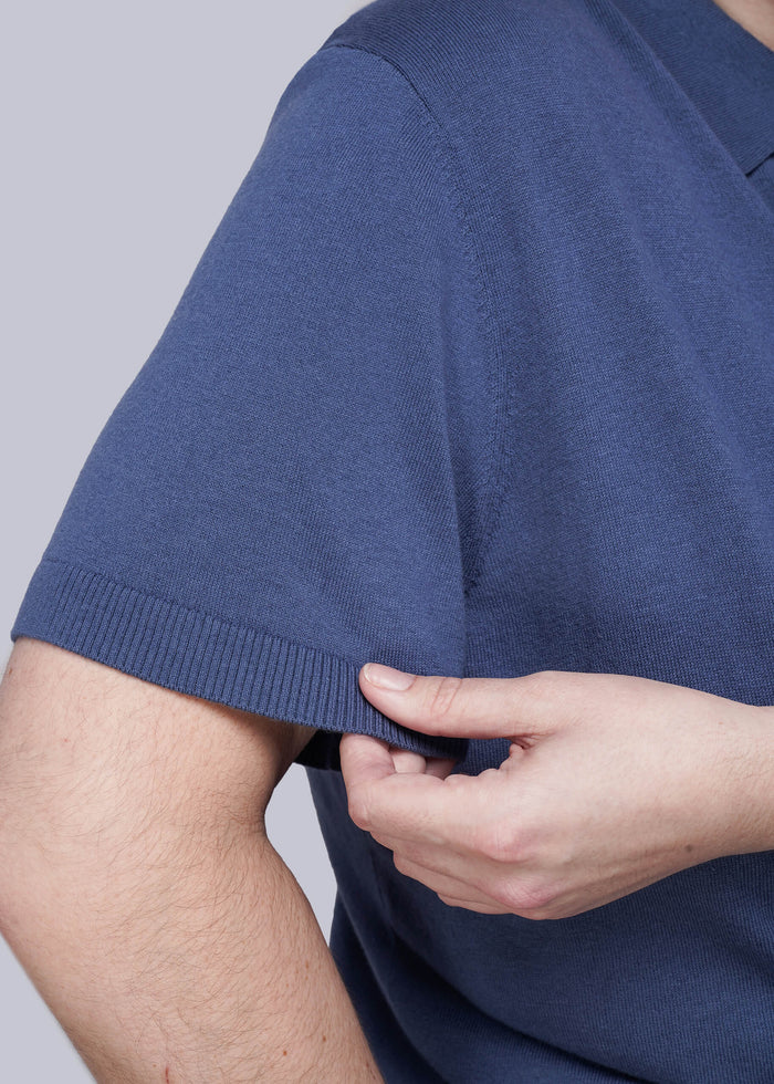 1X=Person wearing a blue shirt with a close-up of the sleeve and hand adjusting it against a gray background