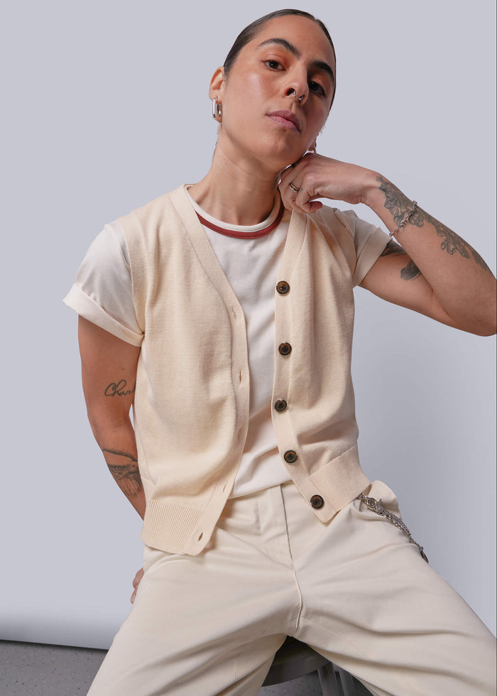 S=Person wearing a beige sweater vest over a white shirt with beige pants against a plain background
