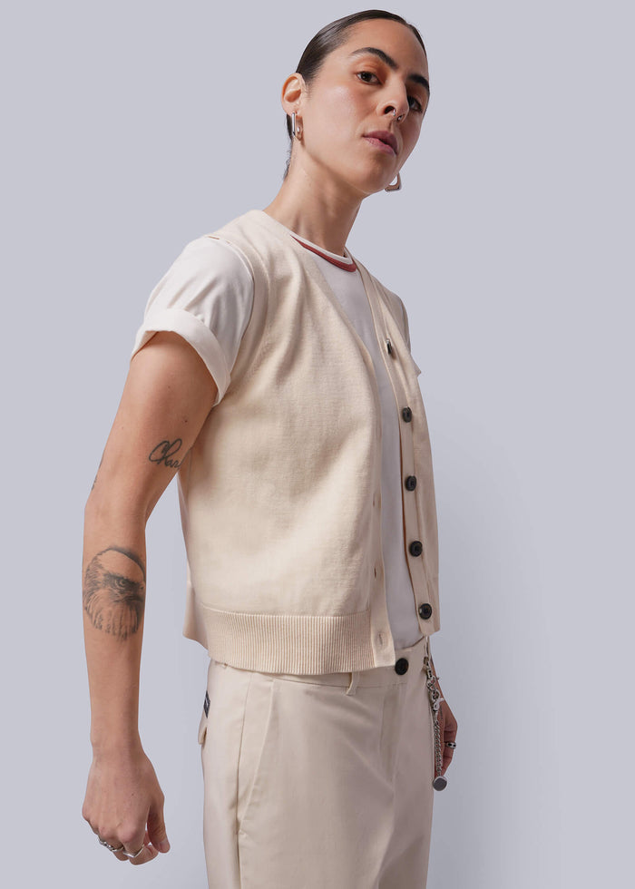 S=Person wearing a beige sweater vest over a white shirt, standing against a plain background.