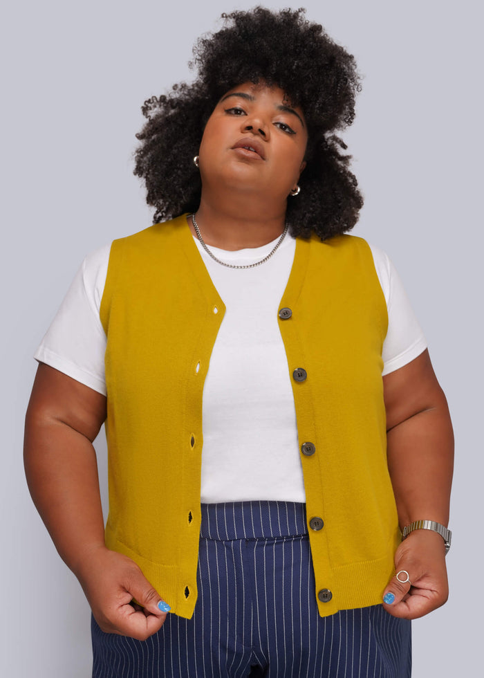 1X=A plus-size model wearing a mustard yellow button-up vest over a white t-shirt and navy blue pinstripe trousers, photographed against a solid light gray background.