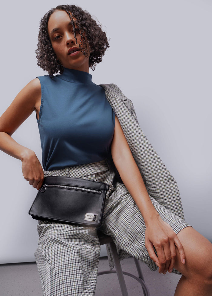 Woman holding a black handbag against a plain background