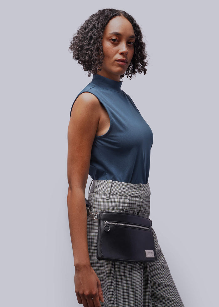 Woman wearing a blue sleeveless top and plaid pants with a black waist bag on a light gray background
