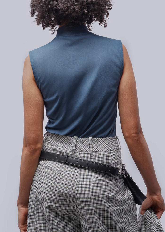 Person wearing a blue sleeveless top and plaid pants with a belt bag, on a plain background