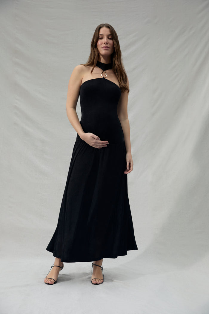 Pregnant woman wearing a black strapless dress with a gold halter accent against a plain background