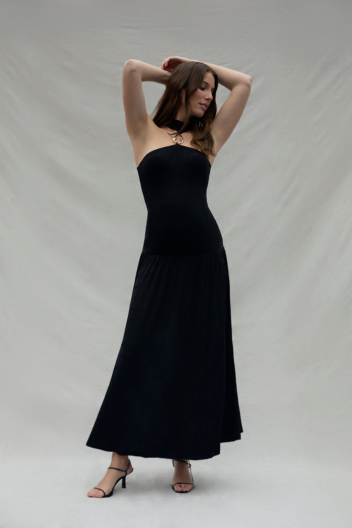 Pregnant woman wearing a black strapless dress with a gold halter accent against a plain background