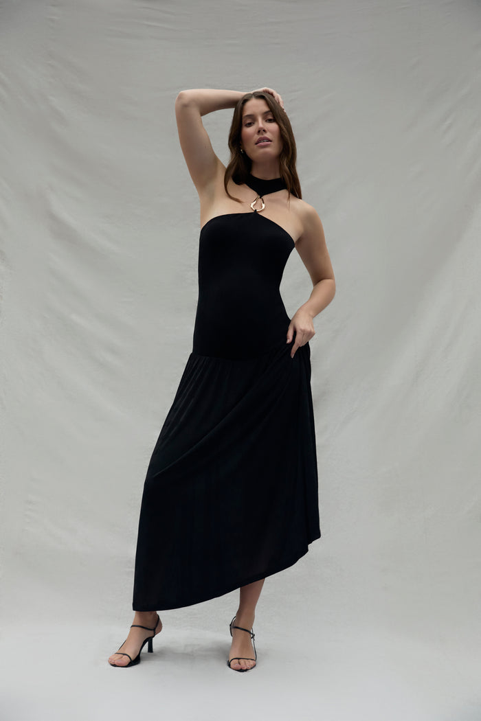Pregnant woman wearing a black strapless halter dress with a gold halter accent against a plain background