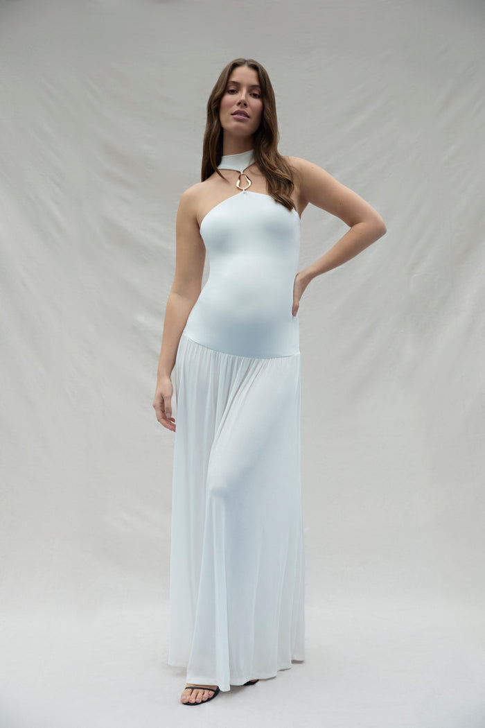 Pregnant woman wearing a ivory strapless halter dress with a gold halter accent against a plain background