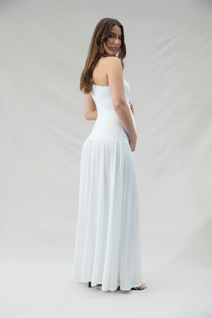 Pregnant woman wearing a ivory strapless halter dress against a plain background