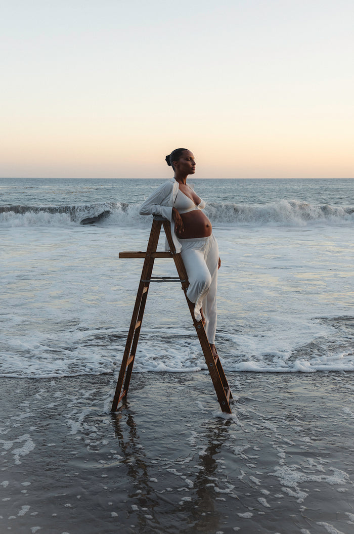 Jasmine Tookes standing on a ladder wearing a white Bumpsuits Luxe Bamboo Pj set