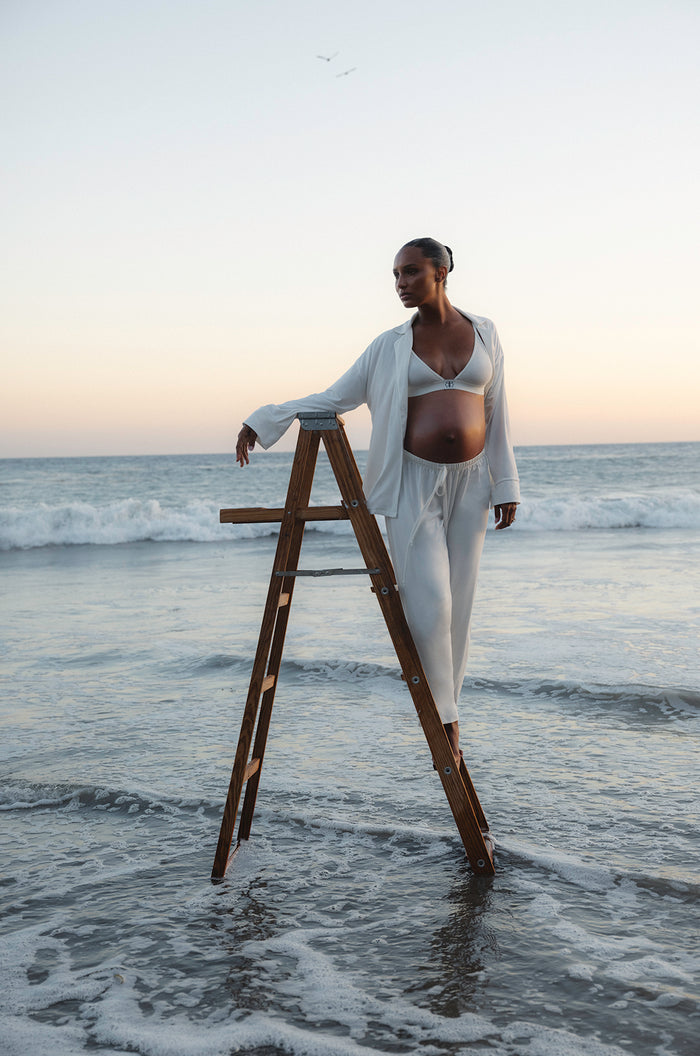 Jasmine Tookes standing on a wooden ladder wearing Bumpsuits White Luxe Bamboo Pj set