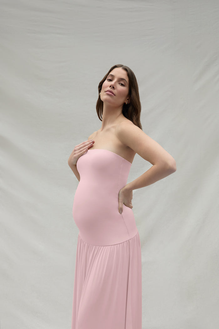 Woman wearing a pink strapless maternity dress against a plain background
