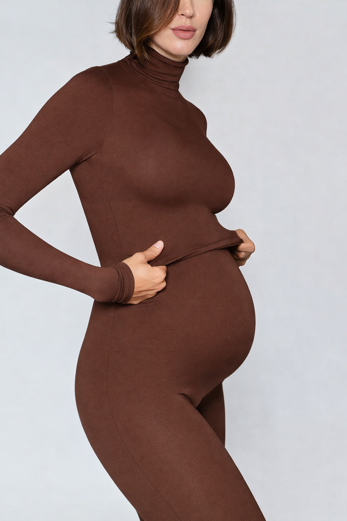 Person wearing a brown turtleneck top and leggings against a plain background