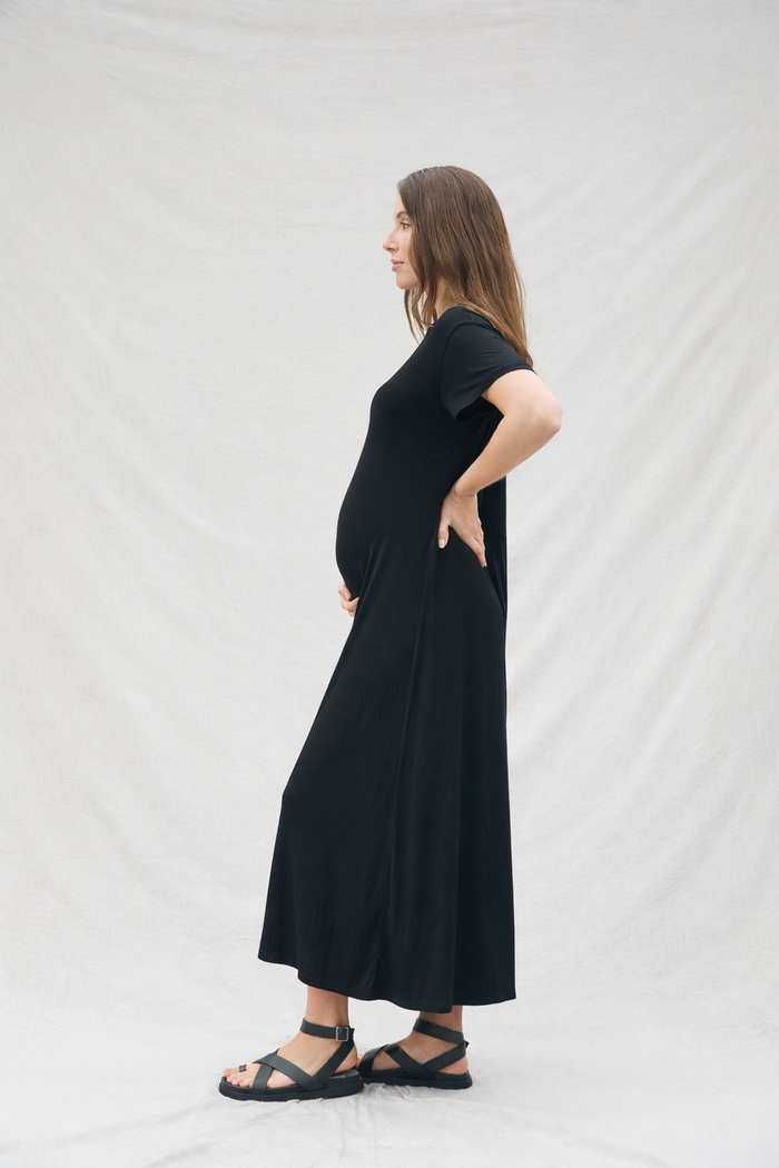 Pregnant woman wearing a black dress standing against a white background